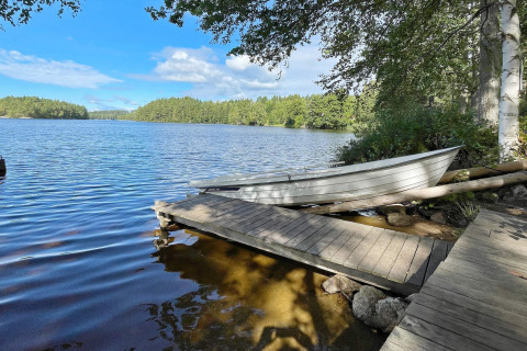 Barca a remi sulla riva del lago vicino a casa vacanza a Rimforsa, Svezia, con pontile e alberi sullo sfondo.