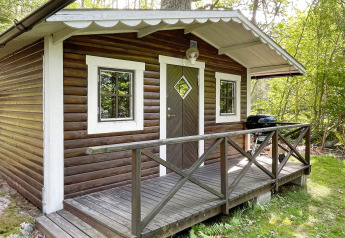Træhytte med veranda i skovområde, set fra forsiden, beliggende ved ferieboligen i Rimforsa, Sverige.