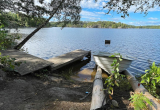 Udsigt til en sø fra en træbro med en robåd ved en hytte i Rimforsa, Sverige, omgivet af natur.