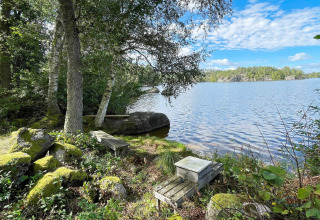 Uitzicht op een rustige meer bij een vakantiehuis in Rimforsa, Zweden, met bankjes en bomen ervoor.