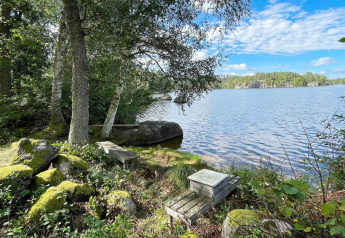 View of a tranquil lake at a holiday home in Rimforsa, Sweden, with benches and trees in the foreground.