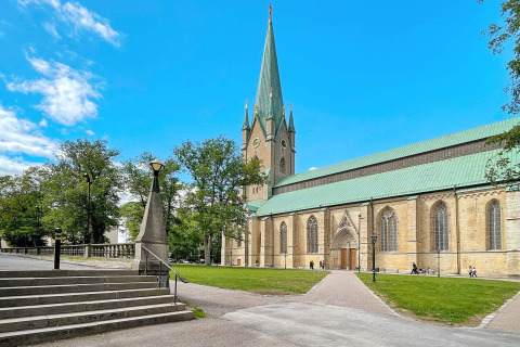 Smuk katedral med grønne tage og høj tårn omgivet af træer og blå himmel i Sverige, fotograferet fra en lodge.