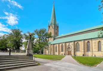 Smuk katedral med grønne tage og høj tårn omgivet af træer og blå himmel i Sverige, fotograferet fra en lodge.