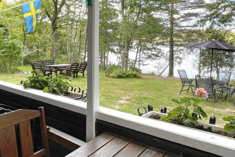 Blick von einer Veranda einer schwedischen Ferienhütte auf Garten, See, Sitzgruppen und Flagge.