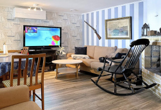 Woonkamer van een vakantiehuis in Rimforsa, Zweden, met tv, bank, schommelstoel en gezellige sfeer.