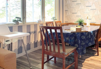 Lichte eetkamer in vakantiehuis in Rimforsa, Zweden, met houten stoelen, kinderstoel en zeilbootdecoratie.