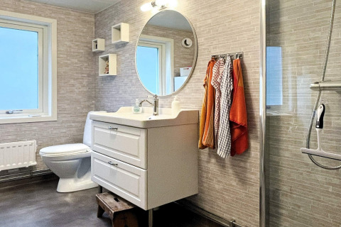Bagno moderno in una casa vacanze a Rimforsa, Svezia, con specchio rotondo e asciugamani colorati.