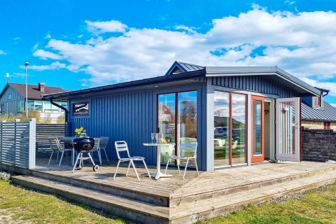 Casa vacanze blu con ampia terrazza in legno, sedie da esterno e barbecue sotto il cielo di Löttorp.