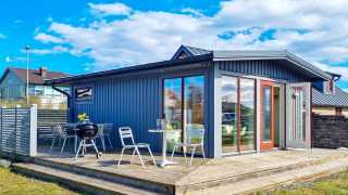 Blå feriebolig med stor terrasse, havemøbler og grill under klar blå himmel i Löttorp, Sverige.