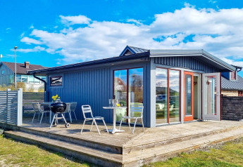 Blaues Ferienhaus mit Holzterrasse, Gartenmöbeln und Grill unter blauem Himmel in Löttorp, Schweden.