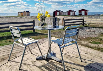 Table et chaises en métal sur terrasse avec vue sur la mer et cabanes rouges à Löttorp, Suède.