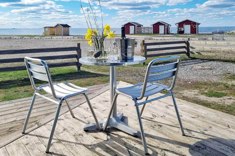 Buitentafel met stoelen op houten terras met uitzicht op zee en rode huisjes in Löttorp, Zweden.