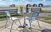 Metalltisch und Stühle auf Terrasse am Strand mit Meerblick und roten Hütten in Löttorp, Schweden.