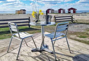 Mesa y sillas de metal al aire libre con vista al mar, flores y cabañas rojas en Löttorp, Suecia.