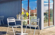 Udendørs terrasse med metalstole, et rundt bord, blomster, isspand og glas ved et sommerhus i Löttorp, Sverige