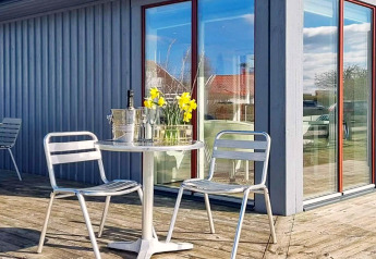 Udendørs terrasse med metalstole, et rundt bord, blomster, isspand og glas ved et sommerhus i Löttorp, Sverige