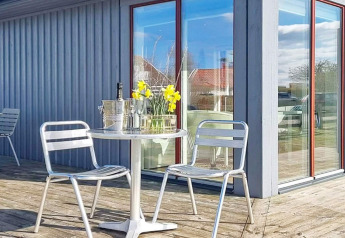 Terraza exterior con sillas metálicas, mesa redonda, flores, cubitera y copas en una casa de vacaciones en Löttorp, Suecia