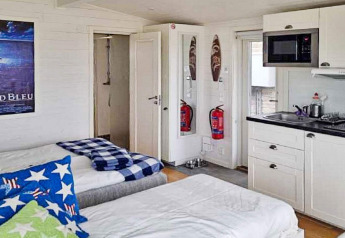 Intérieur d’un gîte 3 personnes à Löttorp, Suède, avec lits, coin cuisine et extincteurs visibles.