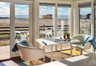 Salon lumineux d’une cabane à Löttorp, Suède, vue sur la mer à travers de grandes baies vitrées modernes.