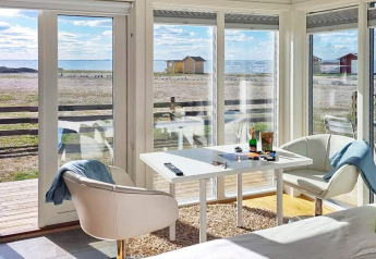 Helles Ferienhauszimmer in Löttorp, Schweden, mit Meerblick durch große Fenster und moderne Einrichtung.