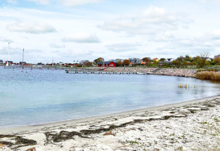 Vue d'une location de vacances à Löttorp, Suède, avec plage de sable, cabanes en bois et eau calme.
