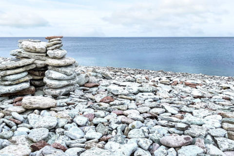 Gestapelde stenen langs het kiezelstrand bij Löttorp, Zweden, met zicht op zee en een bewolkte lucht.
