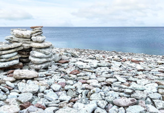Montón de piedras en una playa rocosa en Löttorp, Suecia, con vista al mar tranquilo y cielo nublado.