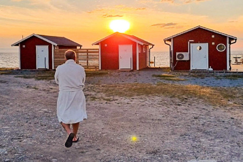 Person im Bademantel läuft auf drei rote Ferienhäuser am Meer zu, bei Sonnenuntergang in Löttorp, Schweden.