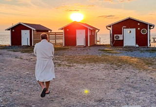 Personne en peignoir marche vers trois cabanes rouges au bord de la mer au coucher du soleil à Löttorp, Suède.