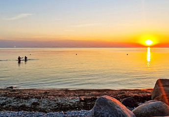 Coucher de soleil sur la plage à Löttorp, Suède, avec des baigneurs et des rochers près du rivage.