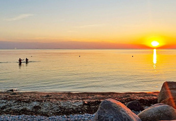 Sonnenuntergang am Strand von Löttorp, Schweden, mit Menschen im Wasser und Steinen am Ufer.