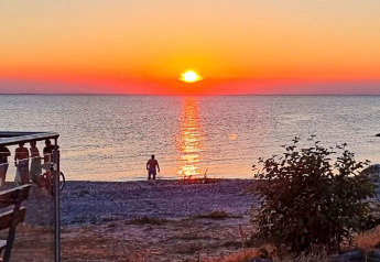 Puesta de sol sobre el mar en la playa cerca de Löttorp, Suecia, con una persona y arbusto delante.