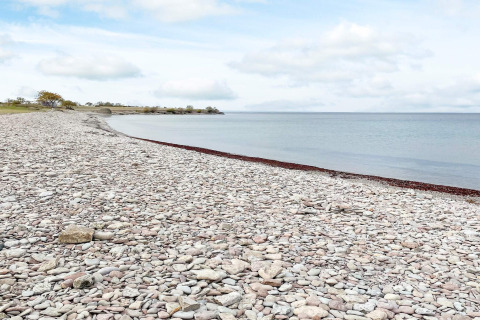 Playa de piedras y mar tranquilo junto a la casa de vacaciones en Löttorp, Suecia, bajo cielo nublado.