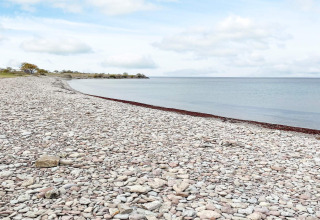 Steiniger Strand und ruhiges Wasser nahe Ferienhaus in Löttorp, Schweden, unter bewölktem Himmel.