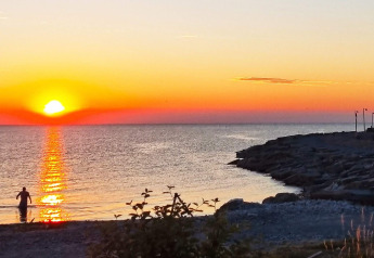 Puesta de sol sobre el mar desde la cabaña 3 person holiday home in LÖTTORP, Suecia, con bañista.