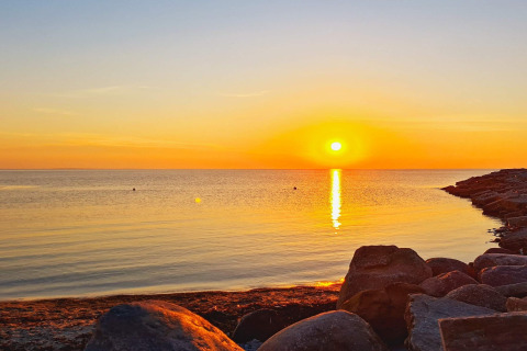 Solnedgang ved havet med store klipper og roligt vand, taget fra 3 personers feriehus i Löttorp, Sverige.