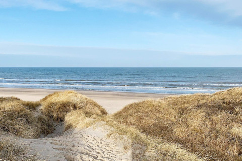 Vista desde las dunas en la playa de Pandrup, Dinamarca, con el mar y el cielo azul al fondo.