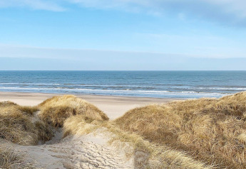 Udsigt fra klitterne ved stranden i Pandrup, Danmark, med hav og klar himmel i det fjerne.