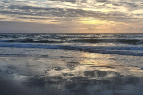 Solnedgang ved stranden i nærheden af 6-personers feriehus i Pandrup, Danmark, med rolige bølger.