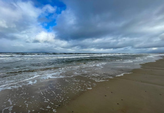 Strand en zee vanaf een vakantiehuis in Pandrup, Denemarken, met golven, nat zand en dreigende lucht.