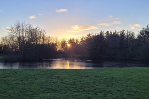 Sonnenuntergang über einem ruhigen See und Wiese am 6-Personen-Ferienhaus in Pandrup, Dänemark.