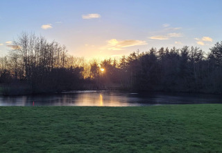 Sonnenuntergang über einem ruhigen See und Wiese am 6-Personen-Ferienhaus in Pandrup, Dänemark.