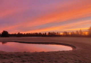 Zonsondergang boven vijver bij 6-persoons vakantiewoning in Pandrup, Denemarken, met oranje lucht.