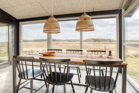 Lichte eetkamer in vakantiehuis in Pandrup, Denemarken, houten tafel, zes stoelen en weids uitzicht buiten.