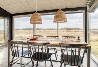 Lichte eetkamer in vakantiehuis in Pandrup, Denemarken, houten tafel, zes stoelen en weids uitzicht buiten.