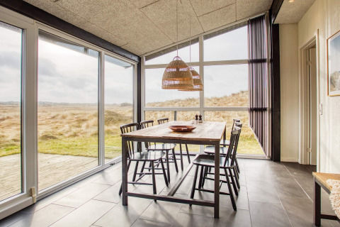 Salle à manger lumineuse avec grandes baies vitrées, vue sur les dunes et table pour six à Pandrup, Danemark.