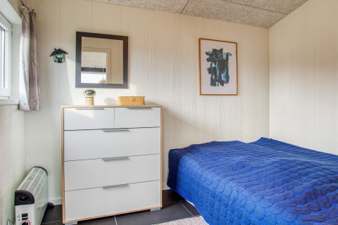 Gezellige slaapkamer in Pandrup vakantiehuis met blauw bed, ladekast, spiegel en abstract kunstwerk.