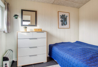 Hyggeligt soveværelse i Pandrup feriehus med blå seng, skuffekommode, spejl og moderne kunst.