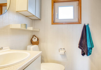 Lichte, eenvoudige badkamer met wastafel, handdoeken, toilet en raam in een vakantiehuis in Pandrup, Denemarken.