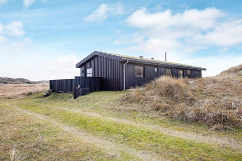 Zwart vakantiehuis voor 6 personen in Pandrup, Denemarken, omgeven door grasduinen en blauwe lucht.